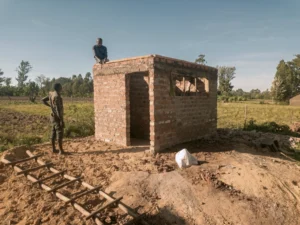 Local masonry workers constructing the brick walls of a community toilet facility in a rural field.