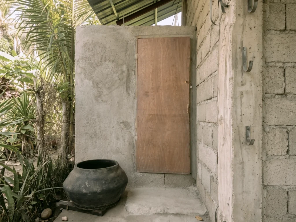 A completed outdoor concrete bathroom structure with a wooden door at a global church planting mission site.