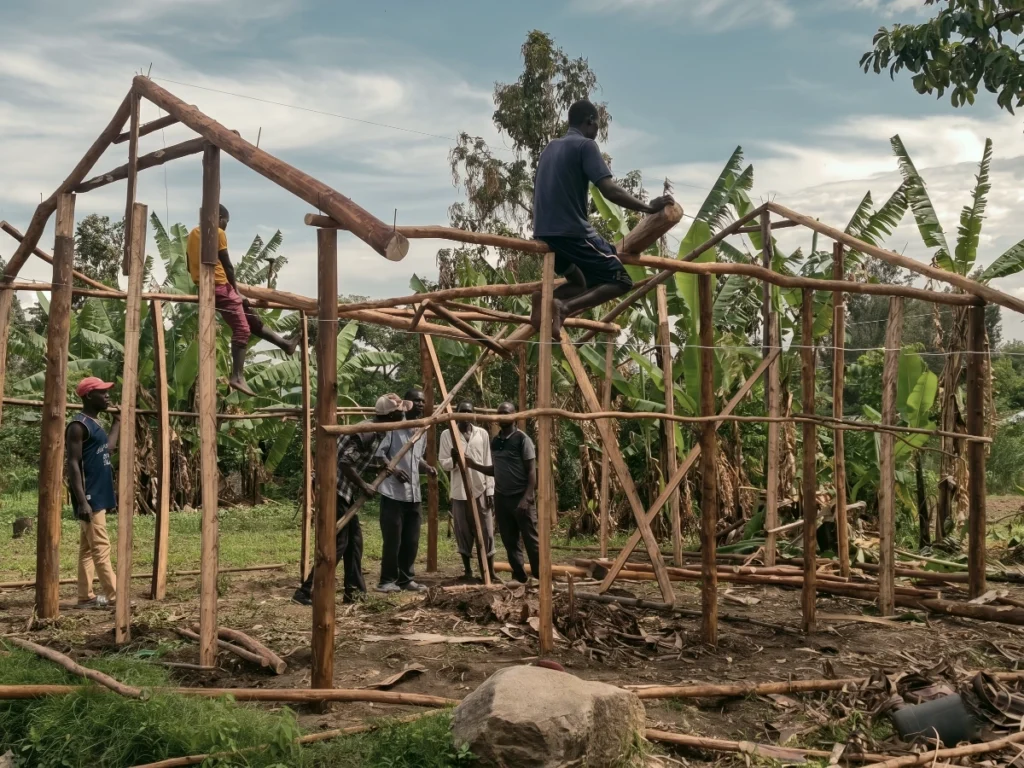 A group of local men collaborate to construct the strong wooden framework of a new house, showing community support for a displaced widow and her sons.