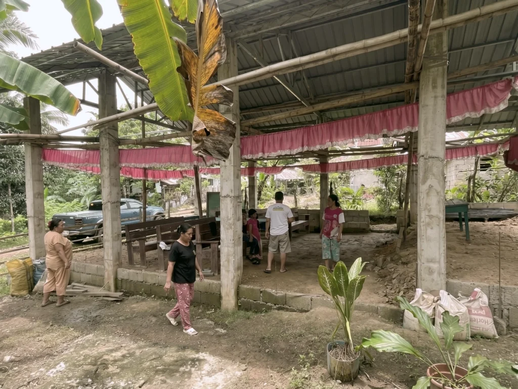 Local community members gathering inside a newly constructed open-air church sanctuary decorated with pink fabric banners.
