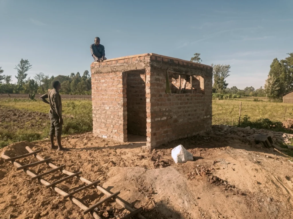 Construction workers building a brick community toilet and sanitation facility in a rural field area.