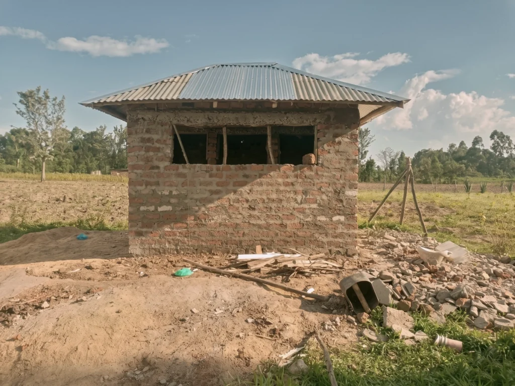 Completed brick structure for a community sanitation facility with a corrugated metal roof in a rural village.