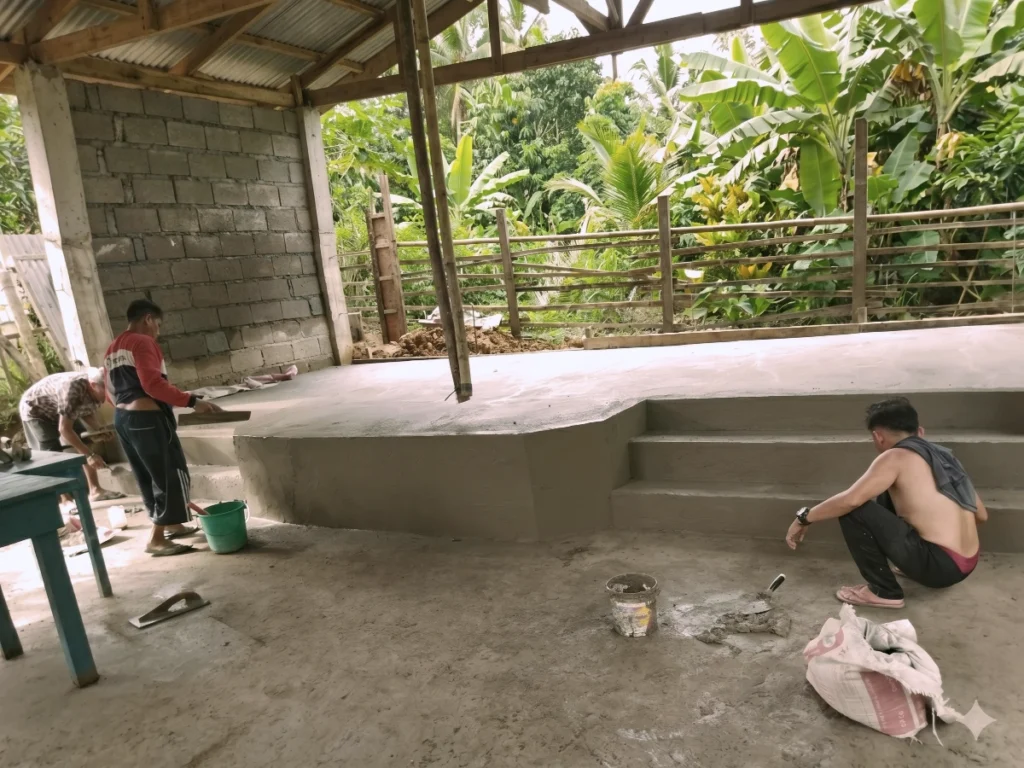 Construction workers laying plaster and finishing wet cement on a new concrete stage inside an open-air church building.
