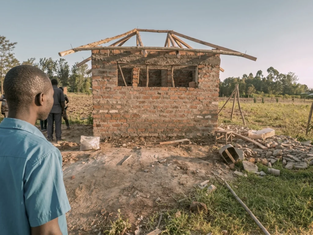 A partially built brick structure with a wooden roof frame, representing the decisive action taken to replace hazardous sanitation infrastructure with a secure, modern facility.