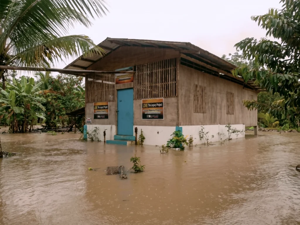 A concrete and wood structure with a bright blue door sits partially submerged in rushing floodwater following the unexpected torrential rains that swept through Maguindanao del Sur.