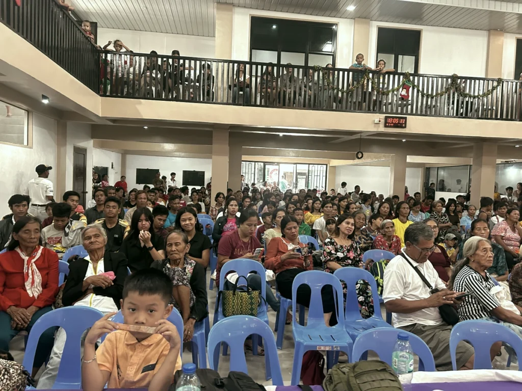 A massive crowd of Filipino community members gathered together across two floors of a large church hall, attentively watching a Bride Arise mission event.