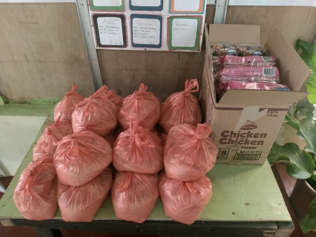 A table full of tied orange bags containing emergency relief supplies and a box of instant noodles, packaged and ready for immediate distribution to Philippine flood victims.